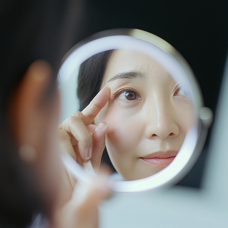 Woman examining her eye area in a mirror after a facelift, checking for facelift side effects such as swelling, tightness, bruising, or changes in skin texture during recovery.
