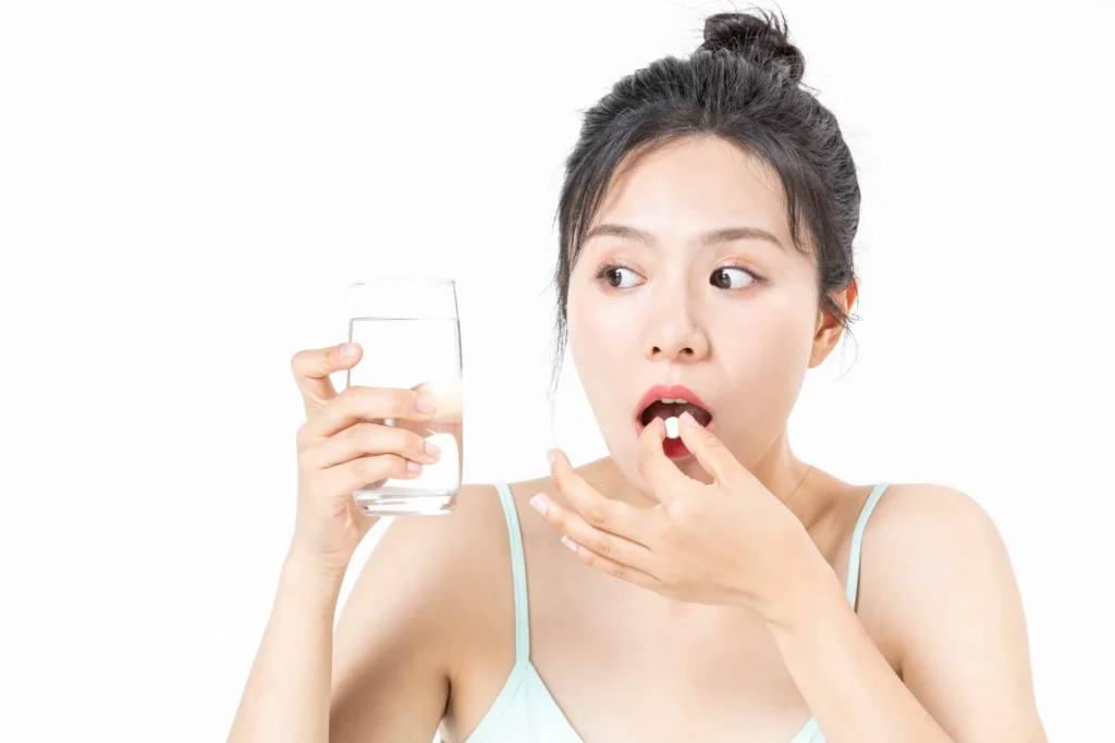 Woman taking prescribed medication with water during postoperative recovery, illustrating pain management considerations related to bras after breast augmentation pain and overall healing care.