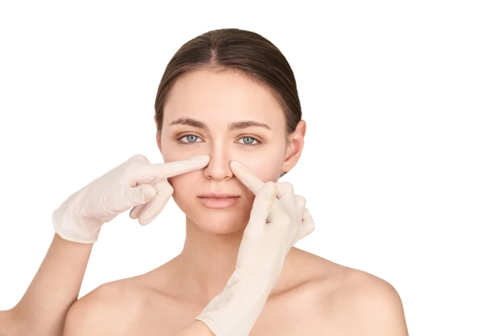 ALT text (English):
Front-facing portrait of a woman undergoing nasal assessment with gloved hands, representing Rhinoplasty In Korea with precise surgical planning and aesthetic evaluation.