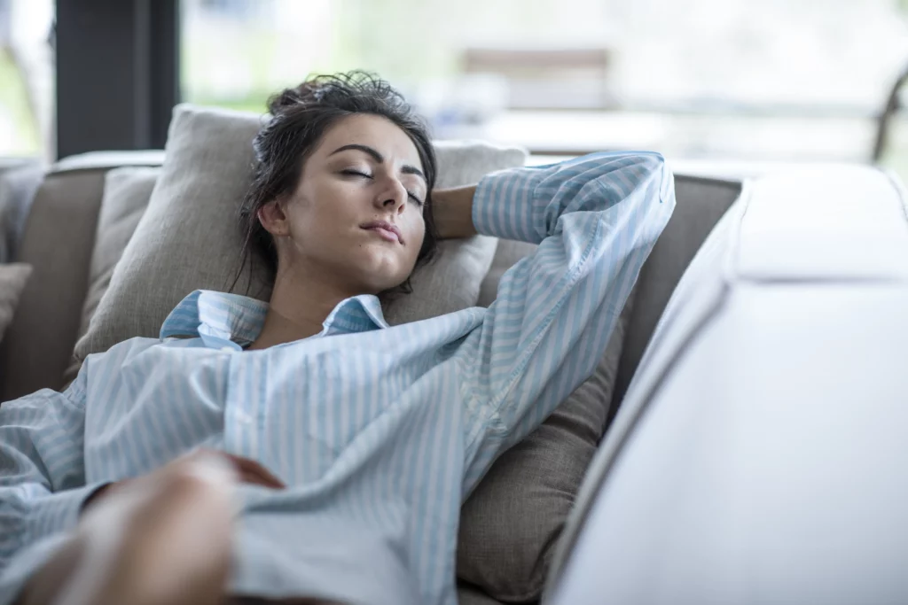 Woman resting on a couch in a loose button-front striped shirt, the ideal breast augmentation recovery pajama.