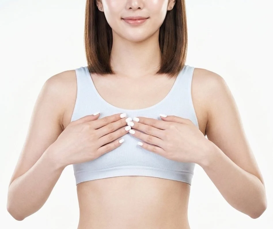 Woman in a light sports bra checking her breast size and symmetry, common reasons patients ask about breast reduction revision surgery.