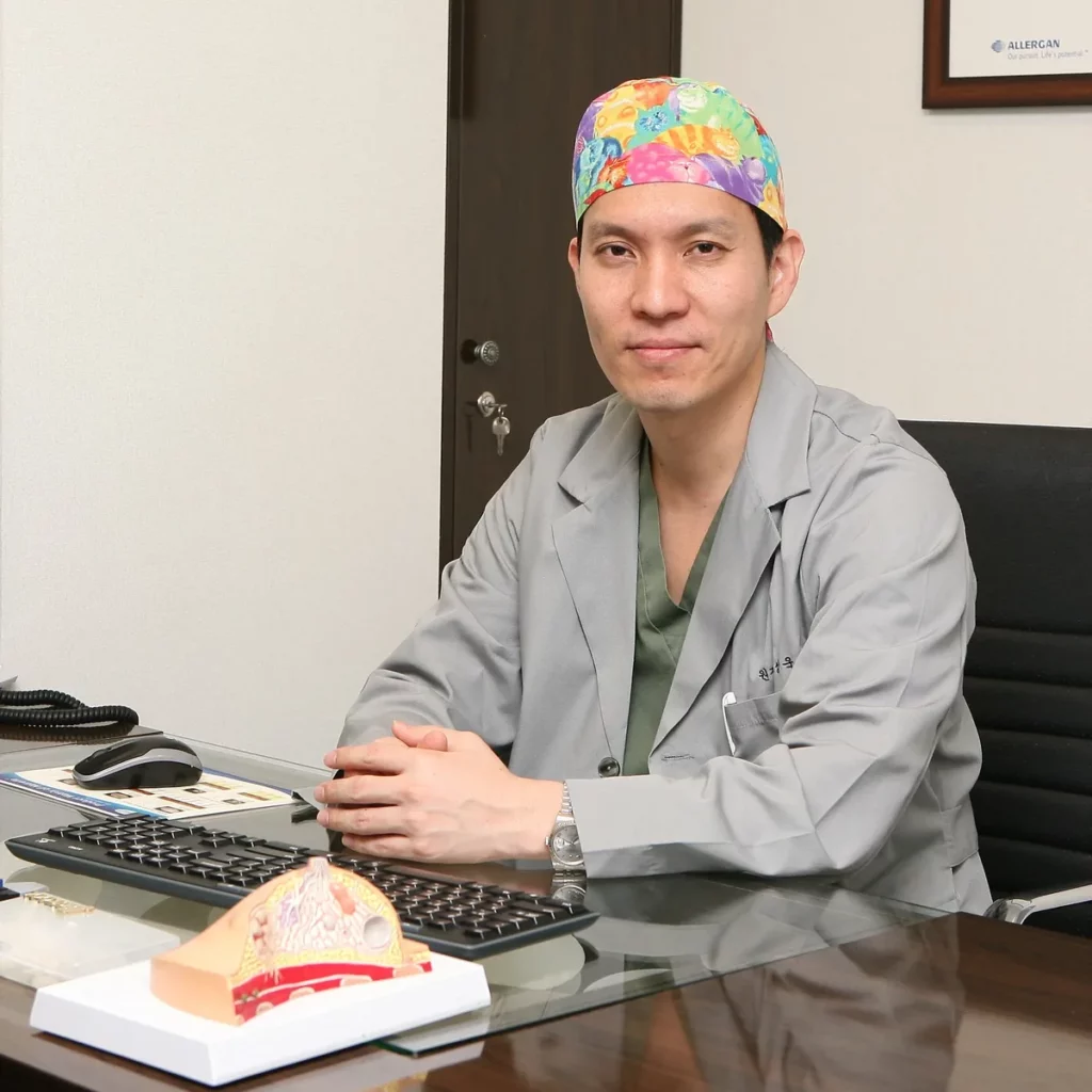 Dr. Lee Sung-wook, board-certified plastic surgeon at MINE, seated in his consultation room with a breast cross-section model while discussing breast augmentation cost in Korea.
