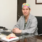 Dr. Lee Sung-wook, board-certified plastic surgeon at MINE, seated in his consultation room with a breast cross-section model while discussing breast augmentation cost in Korea.