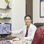 Surgeon explaining breast anatomy on screen to a patient during a consultation for breast implant revision after surgery abroad