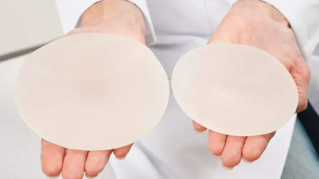 Surgeon holding a larger and a smaller silicone implant, illustrating downsizing breast implants