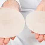 Surgeon holding a larger and a smaller silicone implant, illustrating downsizing breast implants