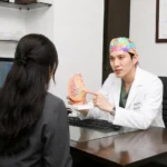 Plastic surgeon explaining the causes of inverted nipple recurrence to a patient using a breast anatomy model during a one-on-one consultation
