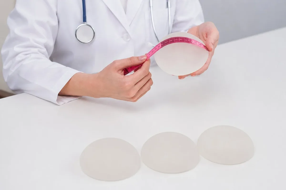 Clinician measuring a round silicone breast implant with a tape measure, with three implants of different projection on the table