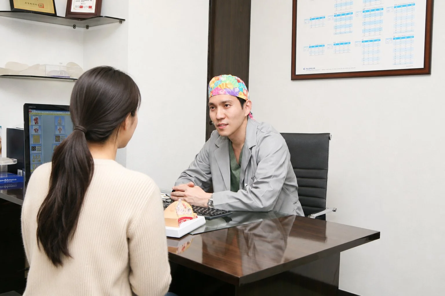 Plastic surgeon discussing breast implant follow-up with a woman at a consultation desk, part of aftercare for implant-based types of breast surgery